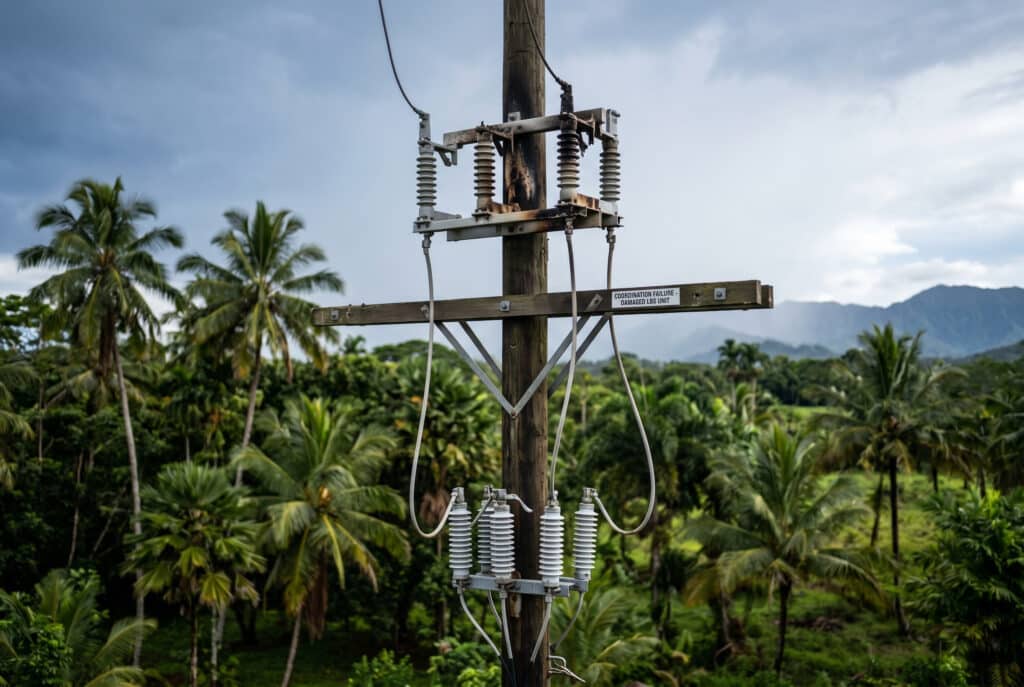 Поврежденный наружный блок LBS на столбе в тропическом пейзаже после грозы, иллюстрирующий неудачную координацию разрядников, показывающий чрезмерную длину проводов и обгоревшее оборудование.